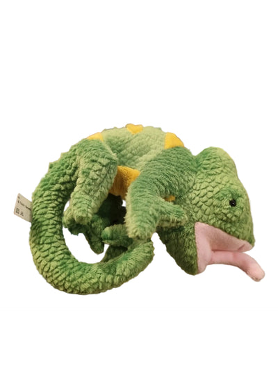 A green plush chameleon toy with yellow spikes and a pink mouth, displayed on a shelf in a store.