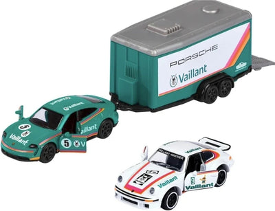 A set of three miniature Porsche racing model cars and a trailer, including a green Porsche 911 with a Vaillant trailer and a white Porsche 911 racing car, on a white background.