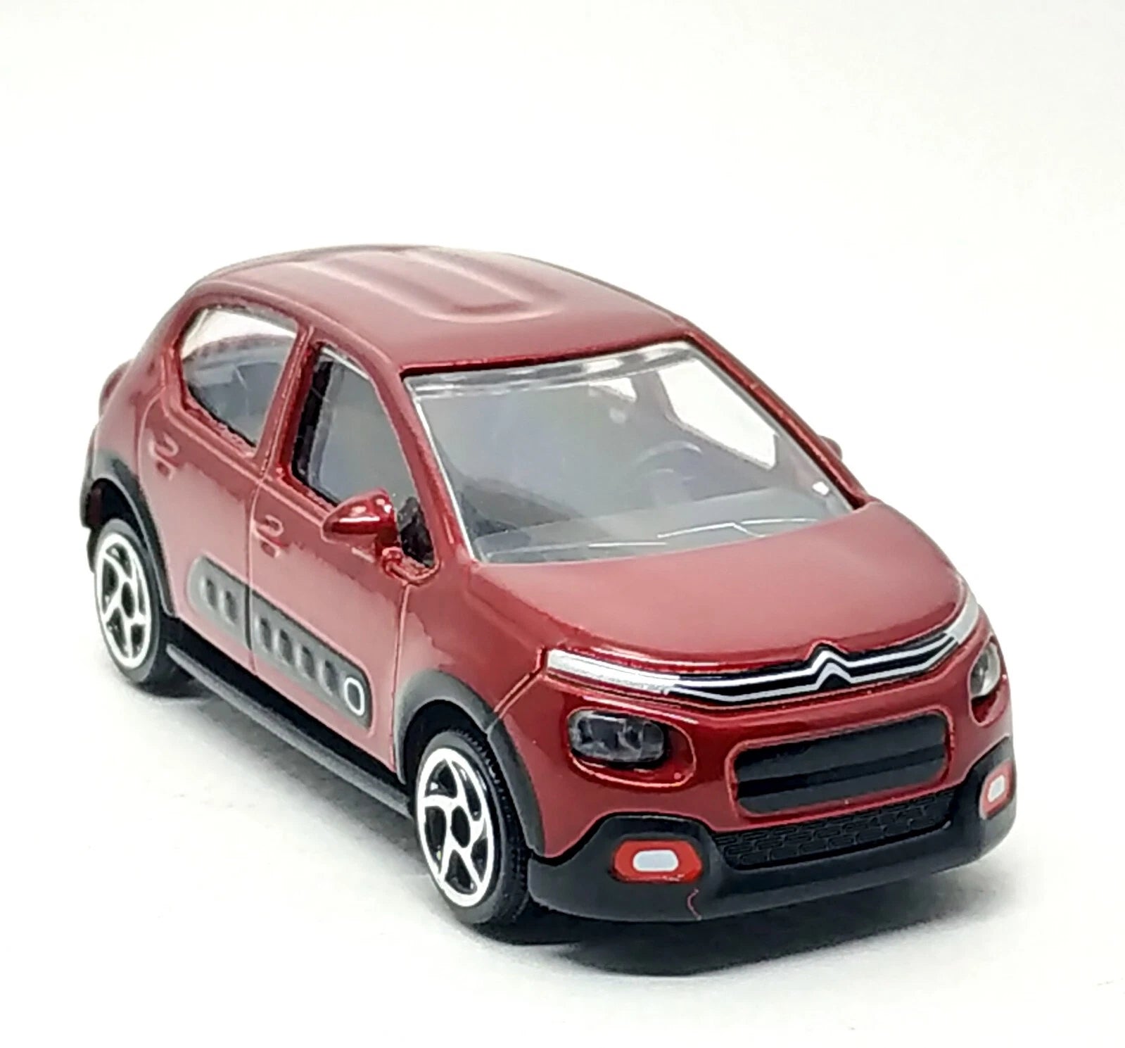 A red Citroën C2 toy car model with black plastic bumpers, wheel arches, and gray side detailing, shown on a plain white background.